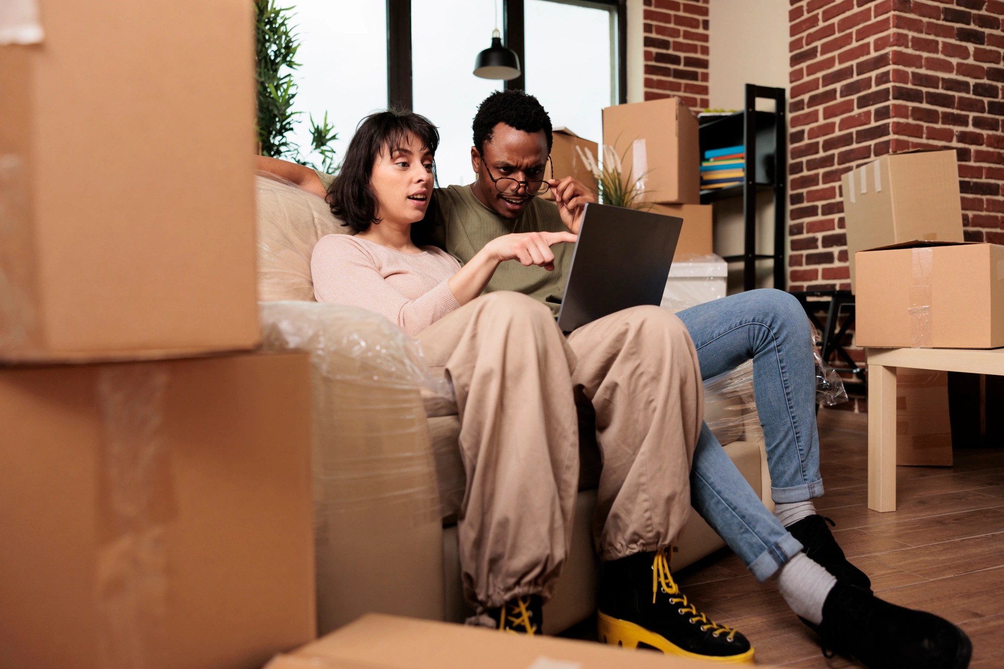 Couple looking at tablet while sitting on couch surrounded by packing boxes