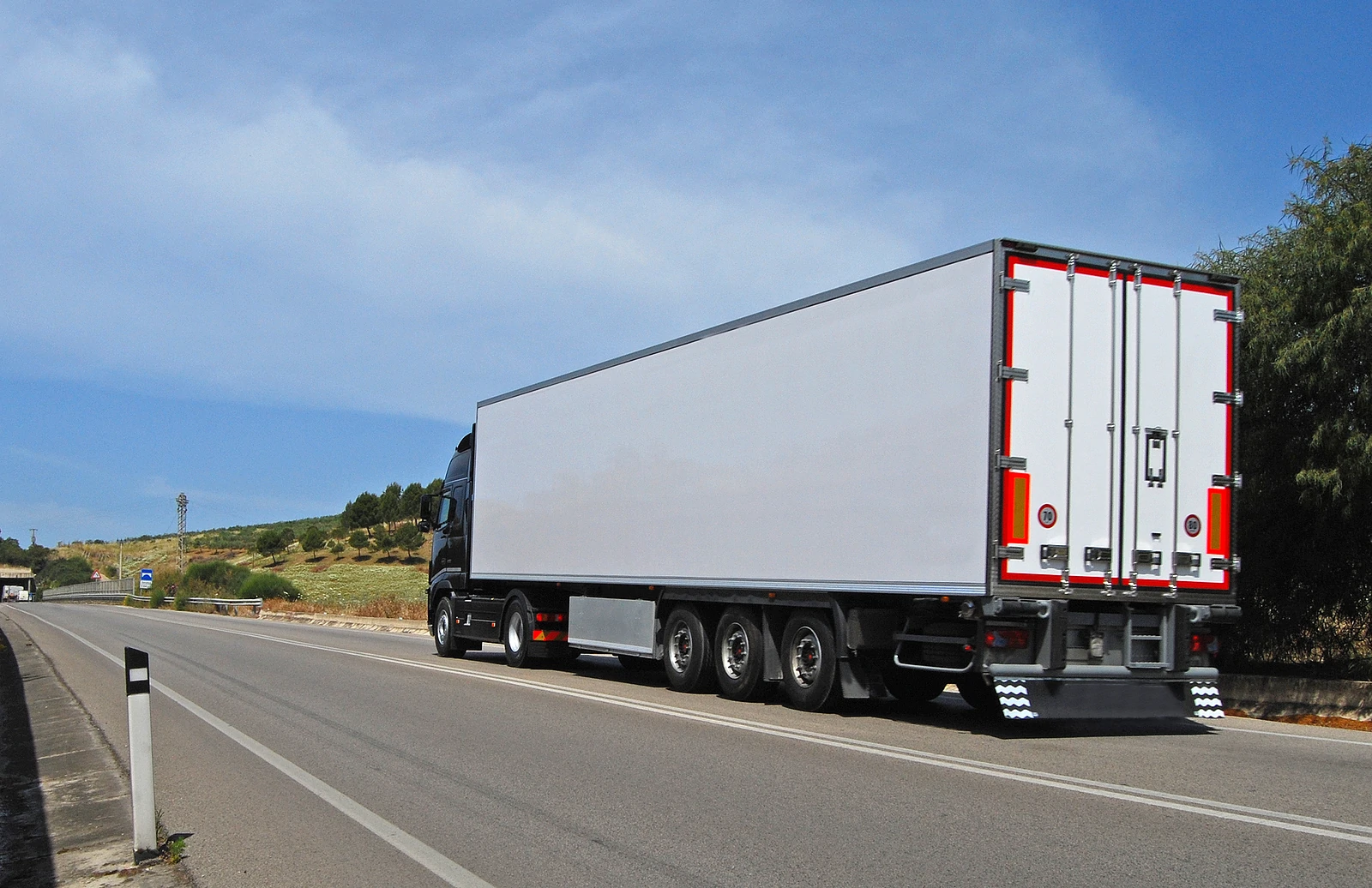 View from behind and to the left of a white semi truck on a highway
