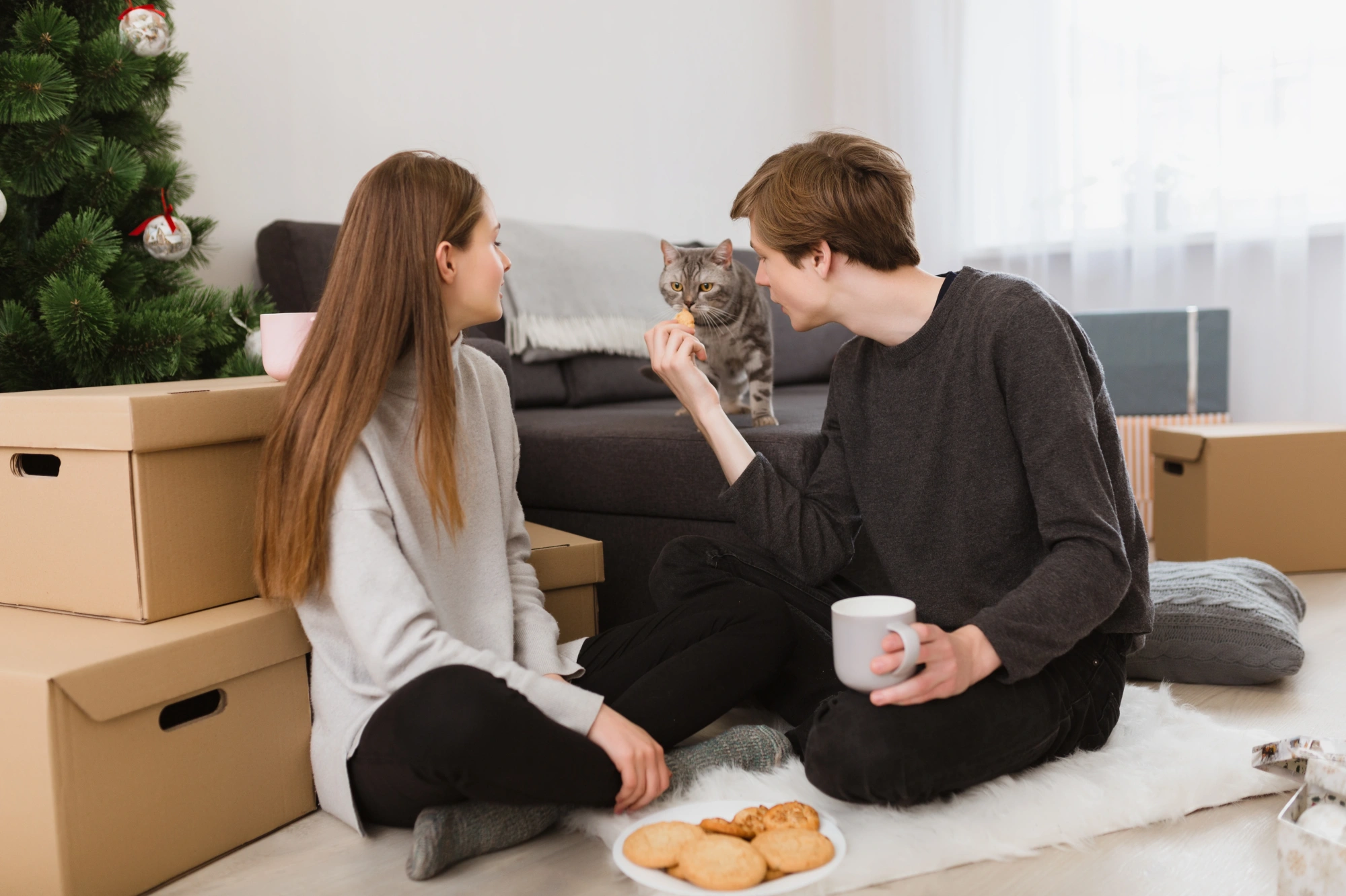 Young couple sitting on floor in home with a cat and cookies